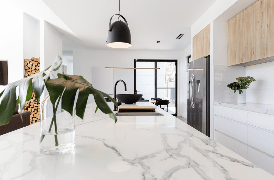 Cuisine moderne avec un plan de travail en marbre élégant, décorée avec une plante et un éclairage suspendu.